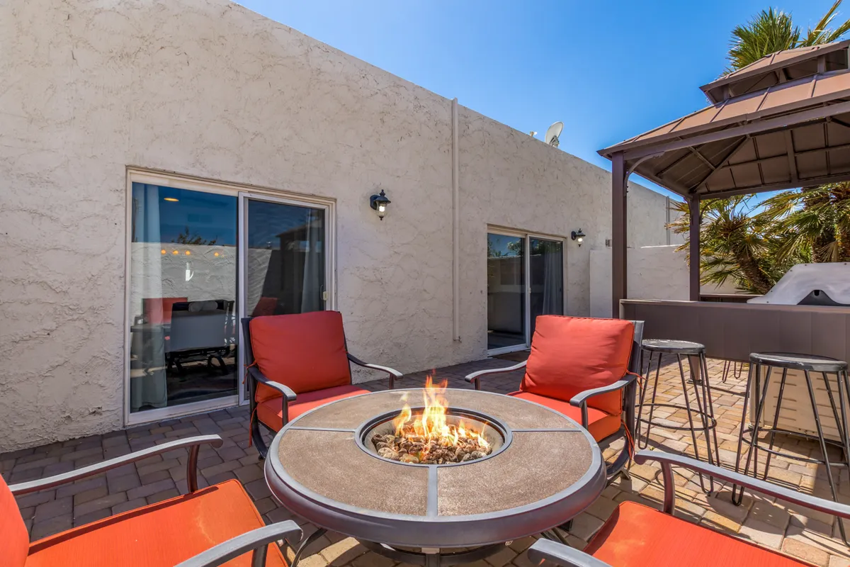 This cozy patio scene features a modern fire pit surrounded by red chairs under a gazebo. The fire pit glows warmly, inviting guests to gather around and enjoy intimate conversations or relax after a busy day. The setup is designed for comfort and socializing, perfectly suited for evenings under the stars.