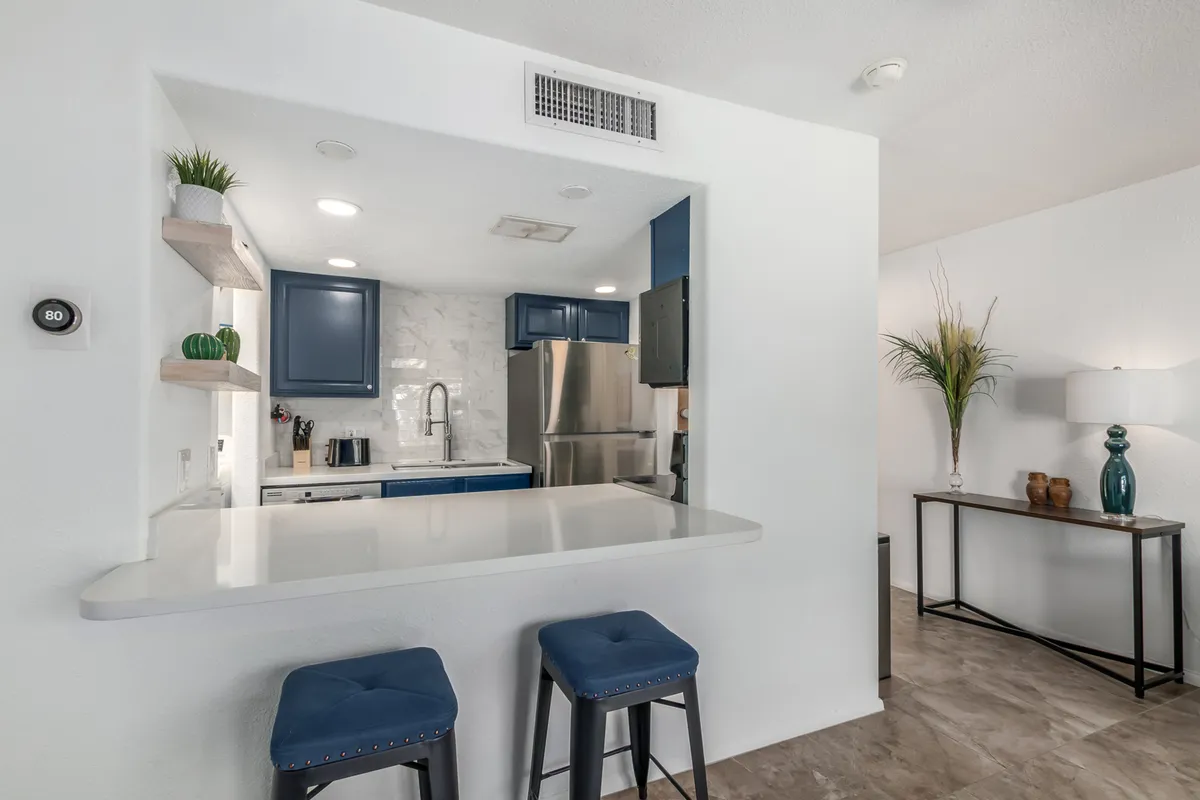 This image showcases a stylish, modern kitchen with a prominent island, blue cabinetry, decorative plant, and bar stools under attractive lighting. The kitchen is clean, well-equipped, and ideal for both meal prep and family gatherings.