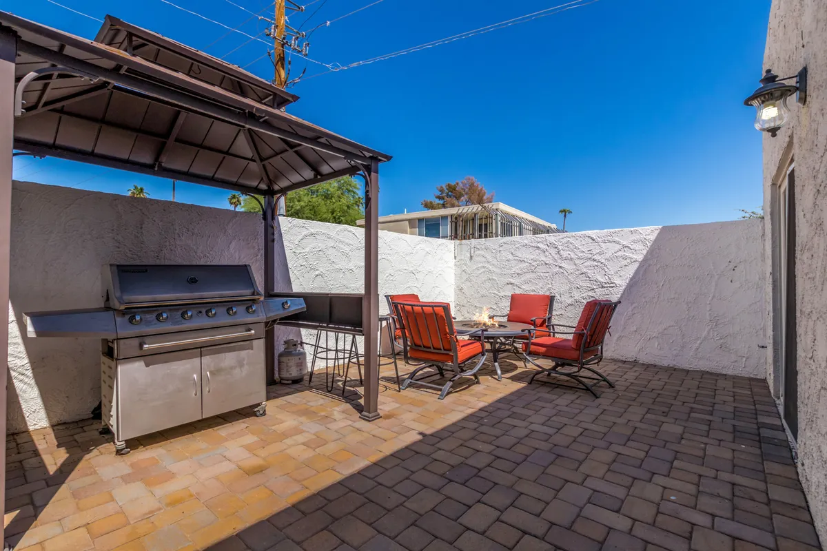 The image displays a private patio area with a grill and outdoor seating set on stylish patio flooring. The space is arranged for casual gatherings, with comfortable chairs positioned around a table, and the grill ready for barbecuing. The atmosphere is relaxed and sociable, suggesting an inviting setting for memorable evenings outdoors.