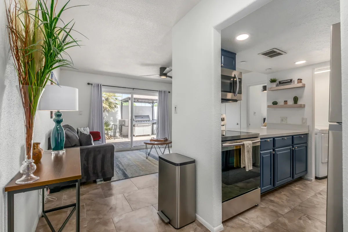 This photo captures an inviting open-plan layout where the kitchen island, dining table, and comfortable sofa are visible. The sliding glass doors allow sunlight to pour in, enhancing the cheerful atmosphere and highlighting the versatility of the space for both relaxation and entertaining.