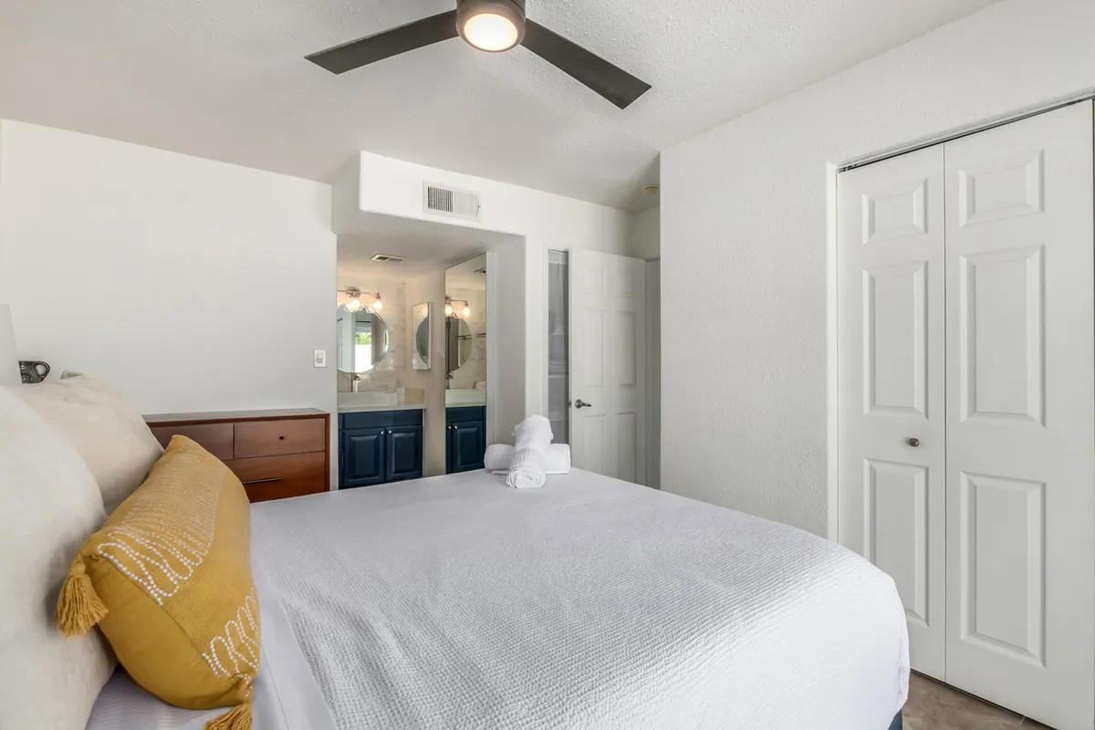A serene bedroom scene with a plush bed adorned with decorative pillows and crisp linens, a vanity with mirrors ideal for morning routines, and bright white walls that amplify natural light. The overall feel is cozy and inviting, with thoughtful touches to enhance relaxation.