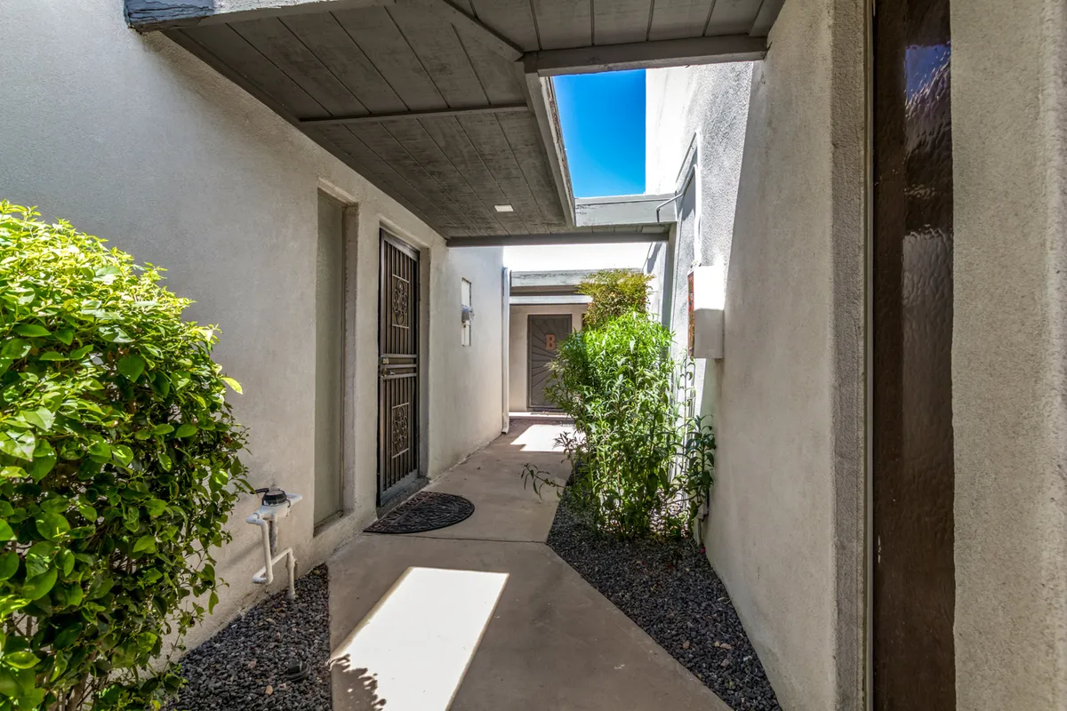 This image displays a welcoming entry pathway lined with green shrubbery and textured walls, leading up to the front door of the property. The scene feels both secure and inviting, with a clear sense of arrival and privacy.